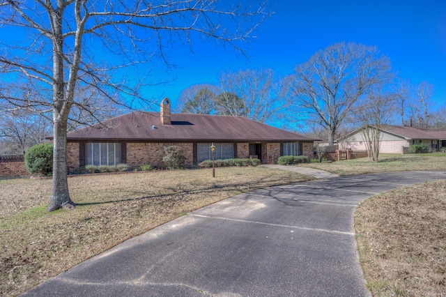 single story home featuring driveway, a front yard, brick siding, and a chimney