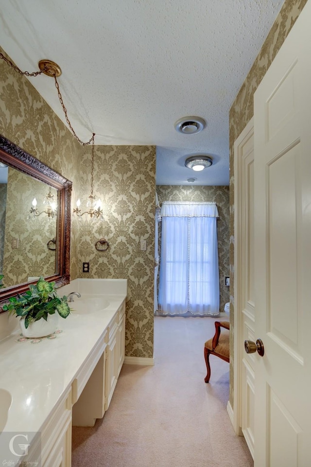 bathroom with a textured ceiling, wallpapered walls, vanity, and baseboards