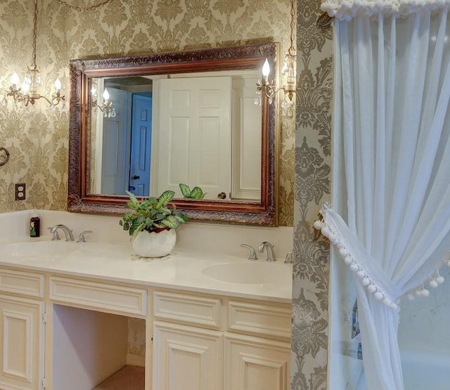 bathroom featuring wallpapered walls, double vanity, an inviting chandelier, and a sink