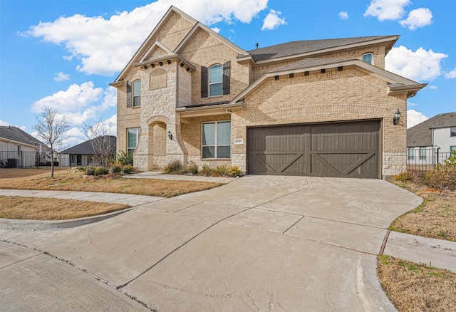 view of front facade with driveway, stone siding, fence, and brick siding