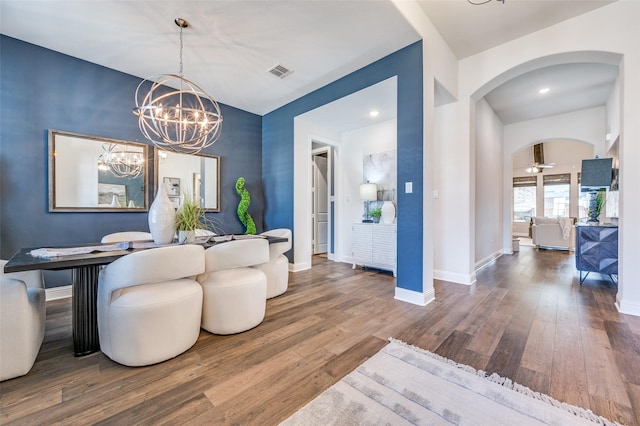 dining area featuring arched walkways, hardwood / wood-style flooring, visible vents, baseboards, and ceiling fan with notable chandelier