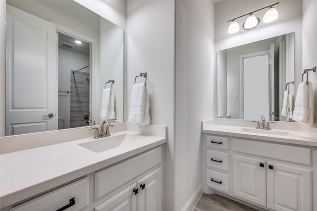 bathroom featuring a shower, wood finished floors, two vanities, and a sink