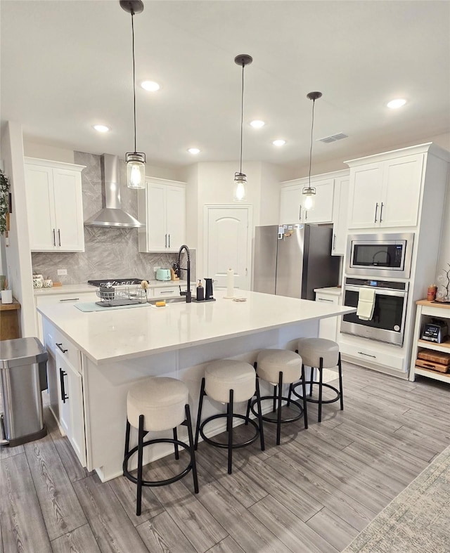 kitchen featuring stainless steel appliances, visible vents, wall chimney range hood, and white cabinetry