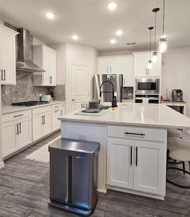 kitchen with visible vents, white cabinetry, appliances with stainless steel finishes, backsplash, and wall chimney exhaust hood