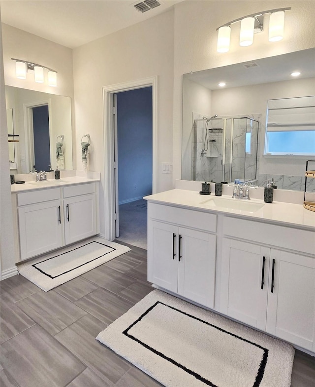 full bath featuring visible vents, two vanities, a sink, and a shower stall