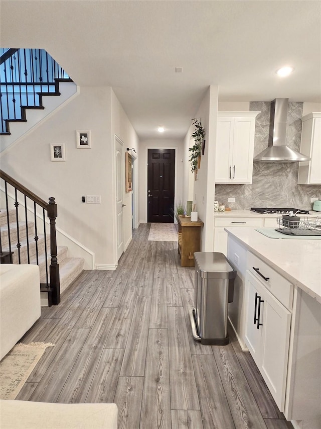 kitchen with tasteful backsplash, light wood-style flooring, wall chimney range hood, gas stovetop, and white cabinetry