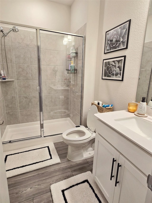 bathroom featuring toilet, a stall shower, wood finished floors, and vanity