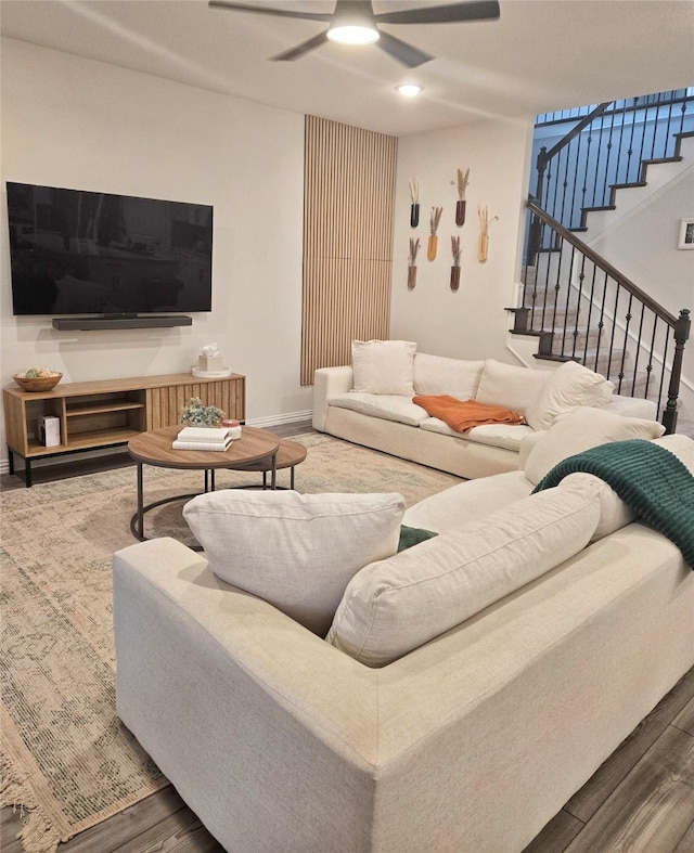 living room with a ceiling fan, stairway, baseboards, and wood finished floors