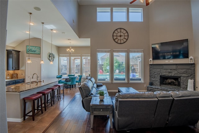 living area featuring ceiling fan with notable chandelier, a fireplace, baseboards, and wood finished floors