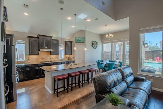 kitchen with a sink, under cabinet range hood, backsplash, appliances with stainless steel finishes, and a breakfast bar area