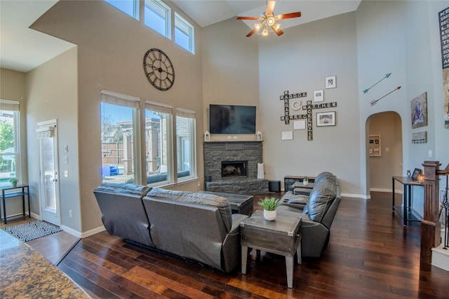 living room featuring a stone fireplace, baseboards, arched walkways, and hardwood / wood-style floors