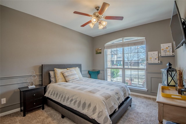 bedroom featuring ceiling fan, wainscoting, and light carpet