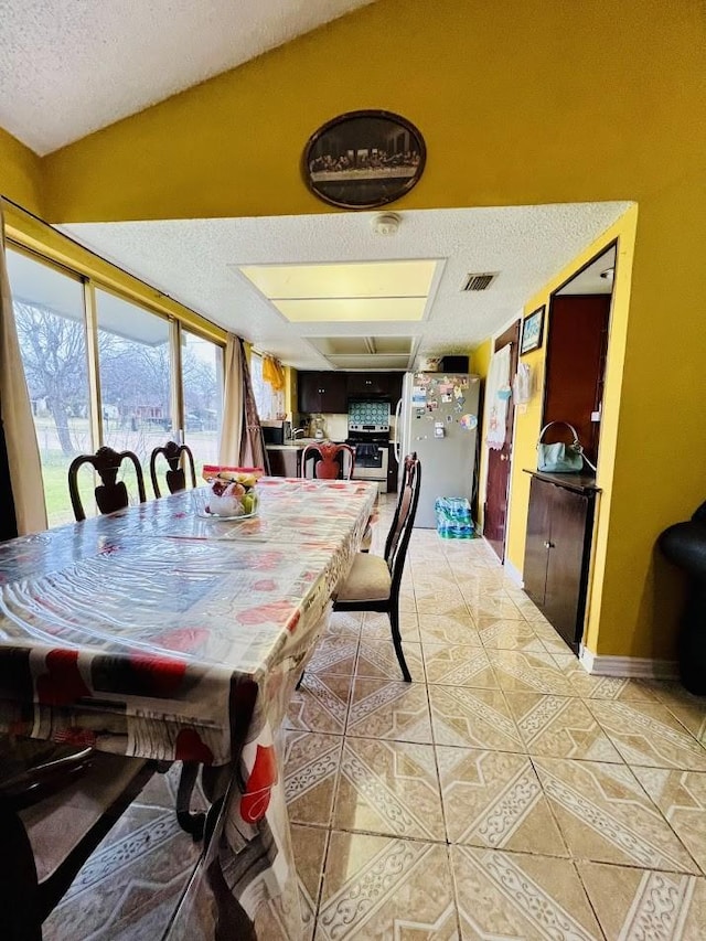 dining space featuring a textured ceiling, light tile patterned flooring, lofted ceiling, and visible vents