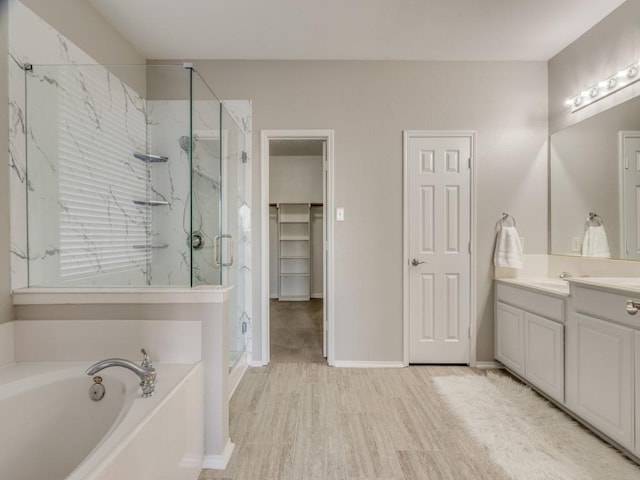 bathroom featuring a garden tub, wood finished floors, vanity, baseboards, and a marble finish shower