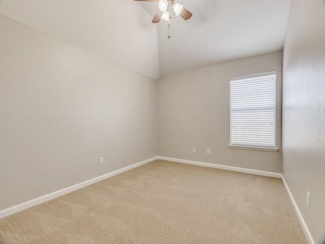 spare room with a ceiling fan, light colored carpet, vaulted ceiling, and baseboards