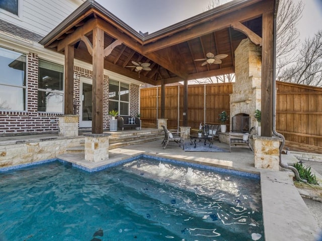 view of pool featuring ceiling fan, a patio, an outdoor stone fireplace, and fence