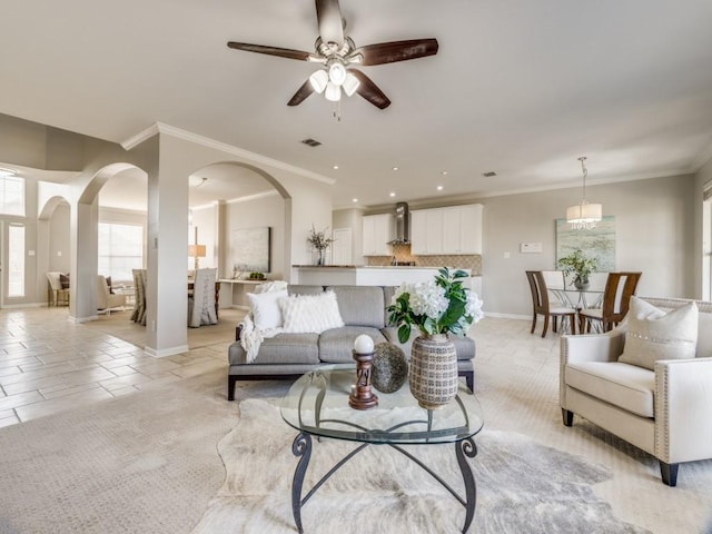 living area featuring visible vents, baseboards, a ceiling fan, arched walkways, and crown molding