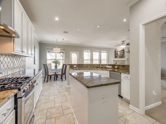 kitchen with tasteful backsplash, appliances with stainless steel finishes, white cabinetry, a kitchen island, and wall chimney range hood