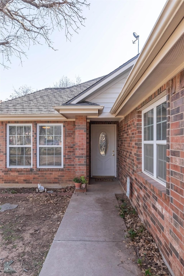 entrance to property with brick siding and a shingled roof