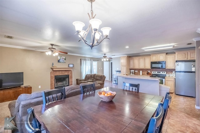 dining space with light tile patterned floors, visible vents, crown molding, a fireplace, and ceiling fan with notable chandelier