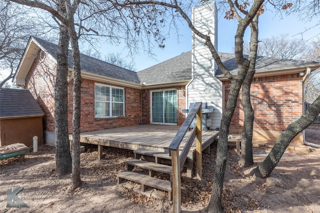 back of property with an outbuilding, brick siding, roof with shingles, a chimney, and a deck