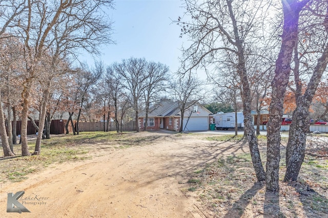 view of front facade with dirt driveway, an attached garage, and fence