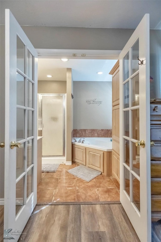 bathroom featuring wood finished floors, french doors, a shower stall, and a bath