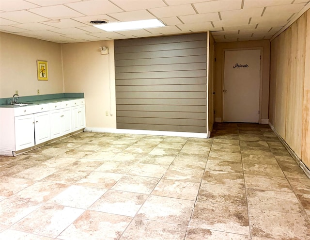 unfurnished room with a paneled ceiling, wooden walls, visible vents, and a sink