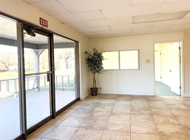 unfurnished room featuring baseboards, a drop ceiling, and light tile patterned flooring