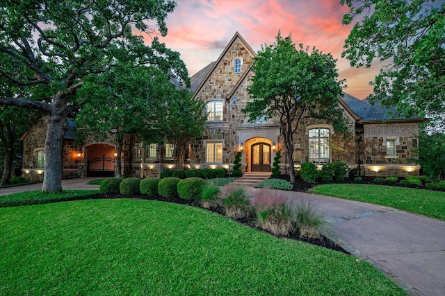 french country style house featuring stone siding, a lawn, french doors, and driveway