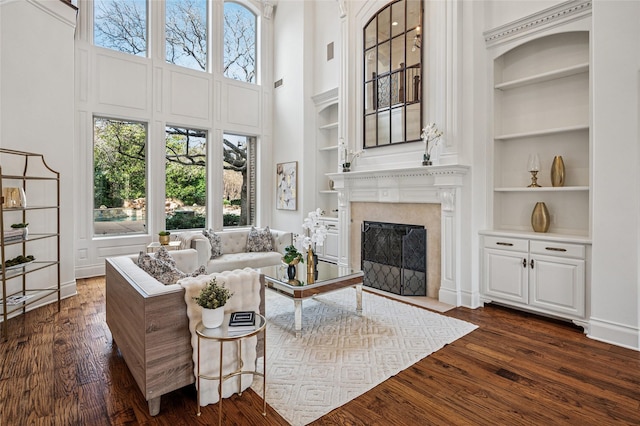 living room featuring dark wood finished floors, built in features, a towering ceiling, and a premium fireplace