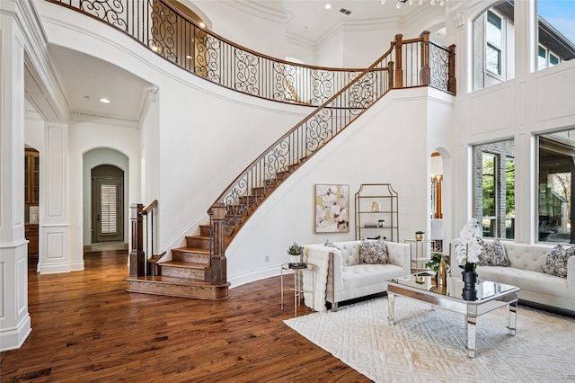 living area with arched walkways, wood finished floors, and crown molding