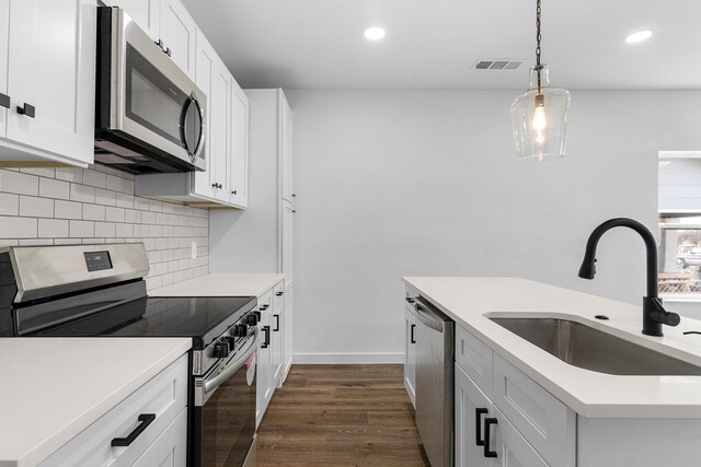 kitchen featuring pendant lighting, decorative backsplash, appliances with stainless steel finishes, dark wood-type flooring, and a sink
