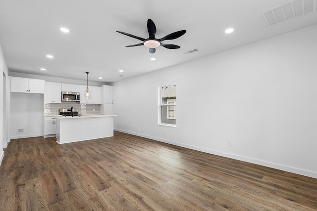 kitchen featuring tasteful backsplash, visible vents, stainless steel microwave, white cabinetry, and a sink