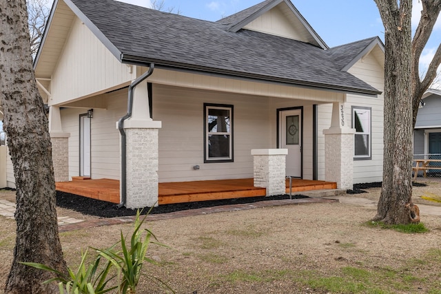 back of house featuring covered porch, a shingled roof, and fence