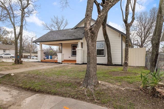 view of side of home featuring a shingled roof, fence, and a porch