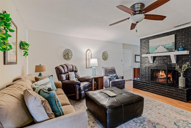 living room with visible vents, a brick fireplace, ceiling fan, a textured ceiling, and wood finished floors