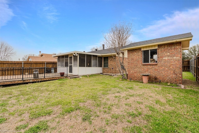 back of house featuring a sunroom, a fenced backyard, brick siding, and a yard