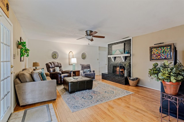 living room with ceiling fan, visible vents, a fireplace, and wood finished floors