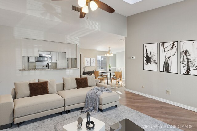 living area with wood finished floors, ceiling fan with notable chandelier, visible vents, and baseboards