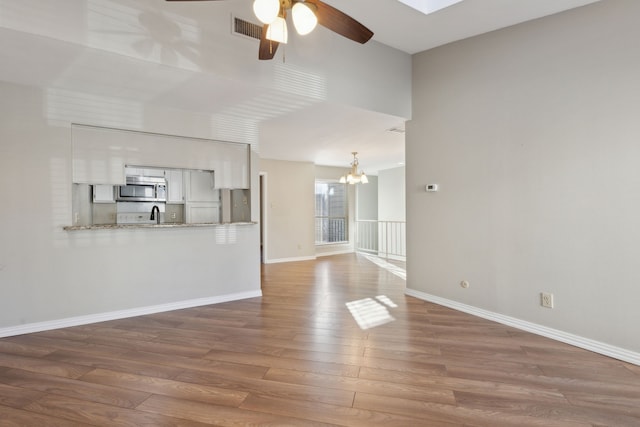 unfurnished living room with visible vents, ceiling fan with notable chandelier, baseboards, and wood finished floors