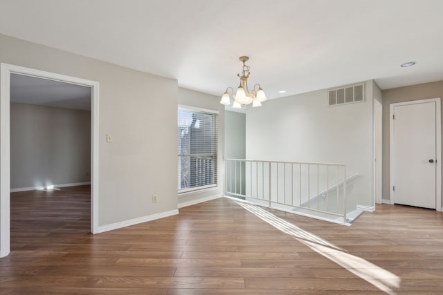 unfurnished room featuring visible vents, baseboards, an inviting chandelier, and wood finished floors