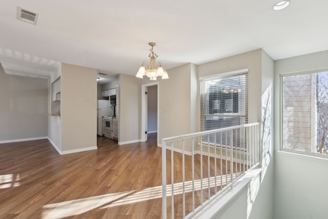 interior space with an inviting chandelier, wood finished floors, visible vents, and baseboards