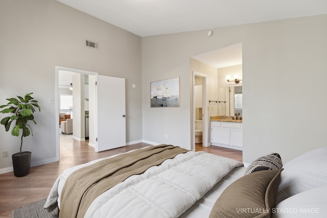 bedroom with visible vents, baseboards, lofted ceiling, light wood-style flooring, and a sink