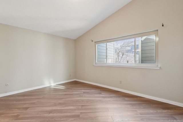 spare room with baseboards, lofted ceiling, and light wood-style floors