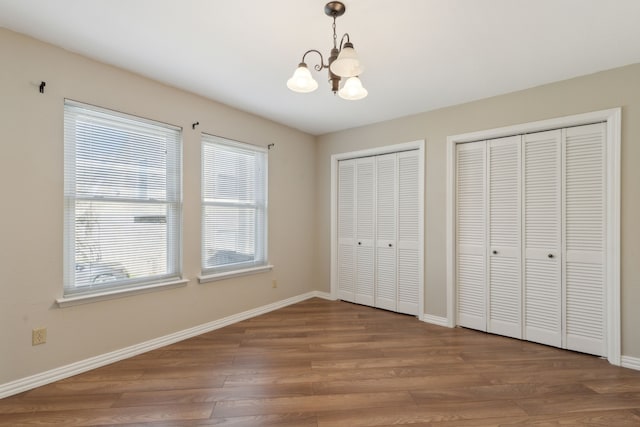 unfurnished bedroom with a notable chandelier, wood finished floors, multiple closets, and baseboards