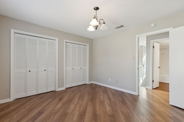 unfurnished bedroom with a notable chandelier, visible vents, multiple closets, and wood finished floors