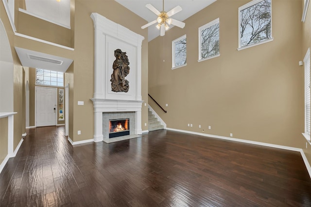 unfurnished living room featuring dark wood-type flooring, a fireplace, a towering ceiling, and baseboards