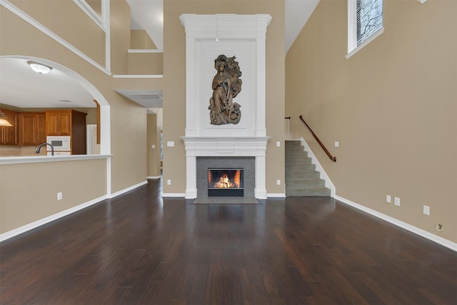 unfurnished living room with a high ceiling, a sink, baseboards, dark wood-style floors, and a tiled fireplace