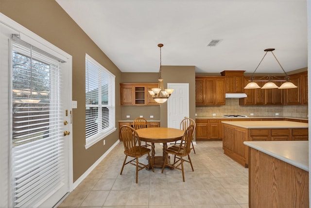 kitchen with tasteful backsplash, visible vents, light countertops, under cabinet range hood, and a chandelier